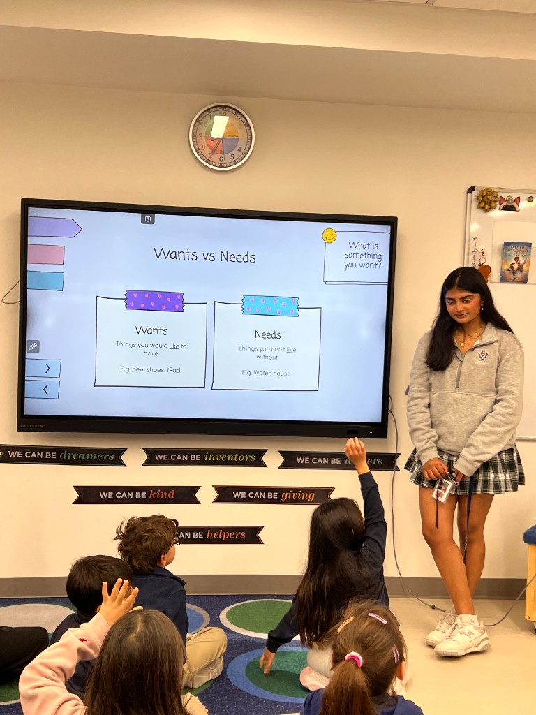 A BizBuddies volunteer leading a lesson while students raise their hands